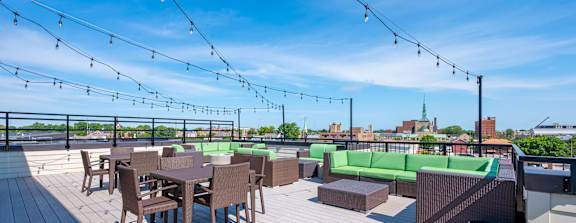 A rooftop patio with wooden flooring, tables and chairs, and string lights.