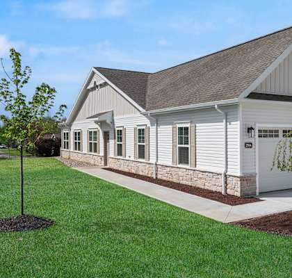 A white building with a brown roof and a tree in front.