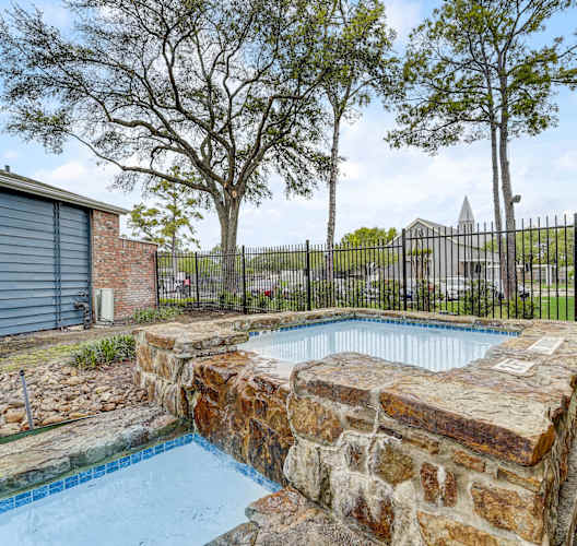 a pool with a stone wall and a fence around it