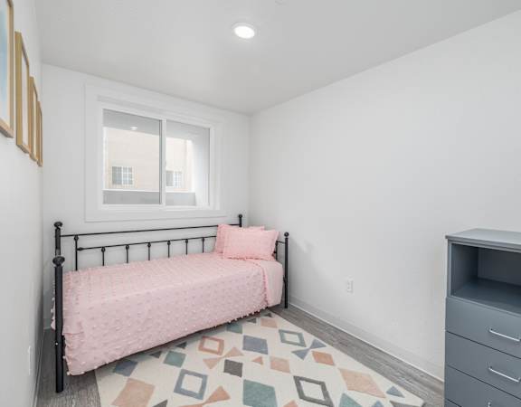 A bedroom with a pink bedspread and a grey filing cabinet.