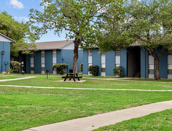 a picnic table sits in a grassy area in front of a blue building  at Sunset Heights, San Antonio, 78209