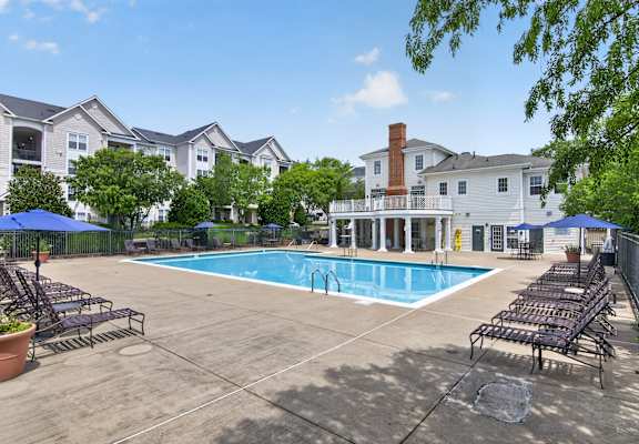 A swimming pool surrounded by lounge chairs and umbrellas in a residential area.