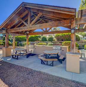 A wooden pavilion with picnic tables is surrounded by a gravel area.