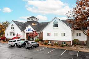 A white building with a black roof and a sign that says "The Shops at Legacy" in front of it.