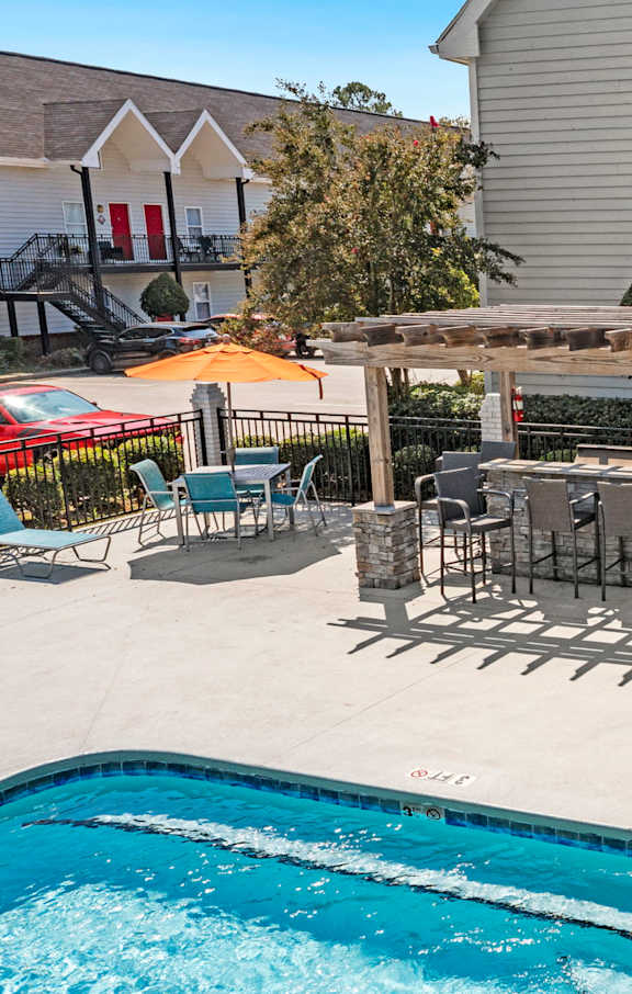 A pool with a table and chairs and a grill in the backyard.