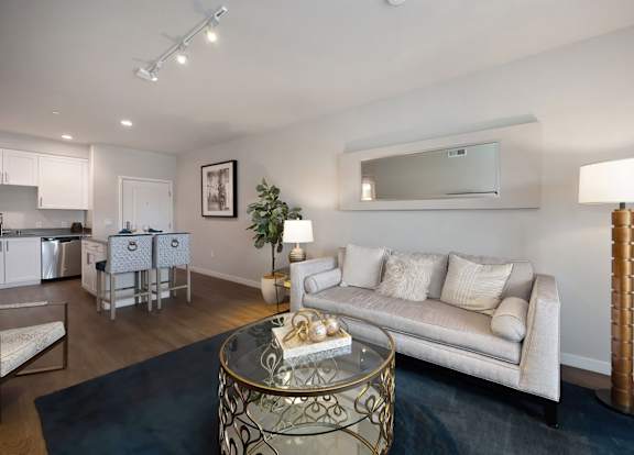 A living room with a beige couch, a glass coffee table, and a black crib.