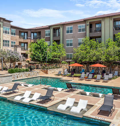A large swimming pool with lounge chairs and umbrellas in front of apartment buildings.