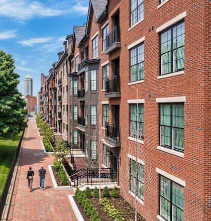 people walking down a sidewalk in front of brick apartment buildings