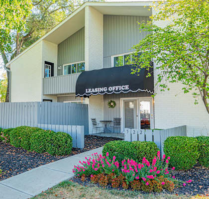 the front of a building with a leasing office sign and flowers