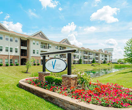an apartment building with a sign in front of a pond and flowers