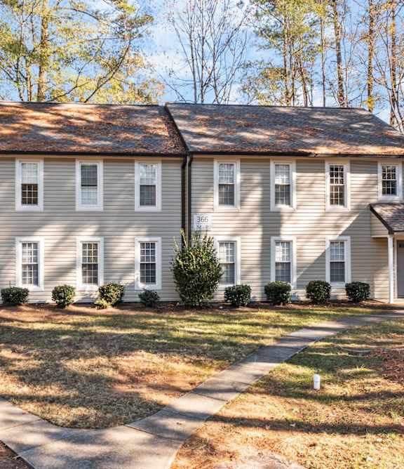 A large house with a grey roof and white walls is surrounded by trees at West Oak Apartments, North Carolina
