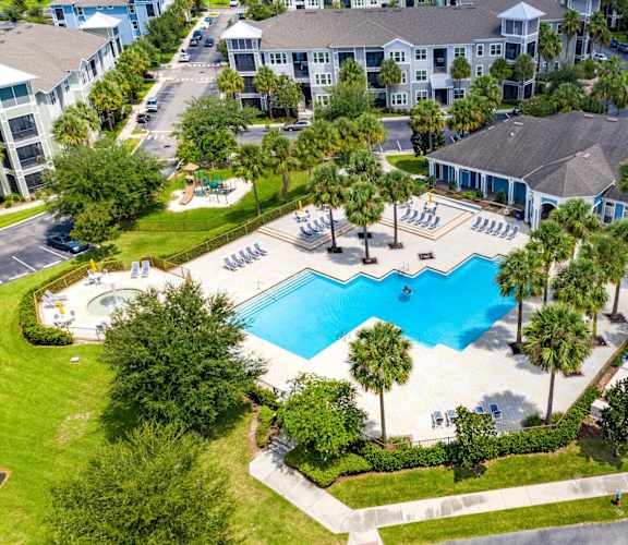An aerial view of a pool surrounded by palm trees and a resort.