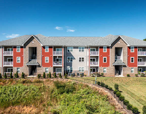 A row of red and grey apartment buildings with green grass in front.