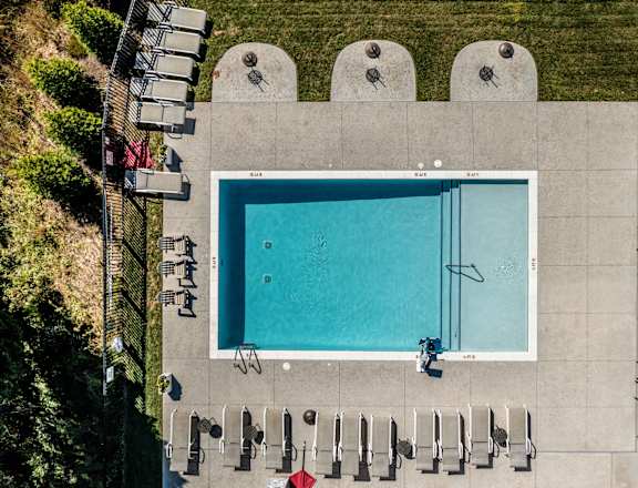 An empty swimming pool surrounded by concrete and lounge chairs.