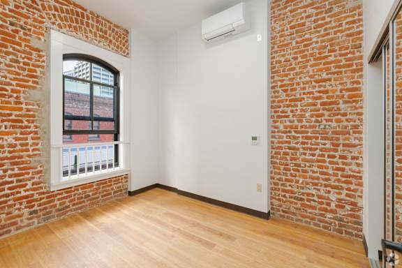 a living room with a brick wall and a window and wood floors