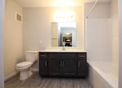 Thumbnail 4 of 14 - A bathroom with a white toilet, a sink with a mirror above it, and a bathtub.