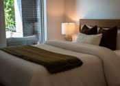 Thumbnail 1 of 8 - A bed with a white comforter and a green throw.