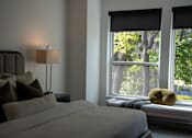 Thumbnail 5 of 8 - A bedroom with a bed, pillows, a lamp, and a window with a view of trees.