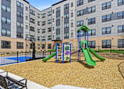 Thumbnail 2 of 22 - A playground with a green slide and a blue slide in front of a building.