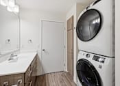 Thumbnail 18 of 22 - A white washing machine is in a laundry room with a sink and mirror.