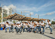 Thumbnail 5 of 6 - A group of people are dancing in front of a wooden structure.