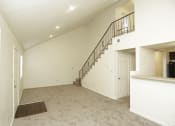 Thumbnail 32 of 36 - Spacious living room with white walls and gray carpeting with a view of a flight of stairs that lead to the loft