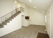 Thumbnail 33 of 36 - Spacious living room with white walls and gray carpeting with a view of a flight of stairs that lead to the loft  and a view of the kitchen with black appliances