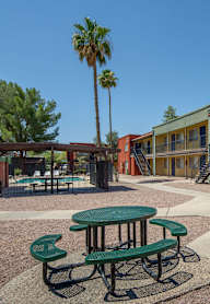 A green table and benches are in the foreground of a courtyard with a building in the background.