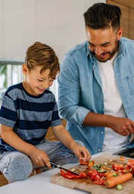 A man and a boy are chopping vegetables on a cutting board.