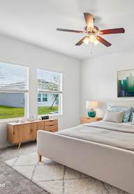A bedroom with a large bed, a ceiling fan, and a painting on the wall.