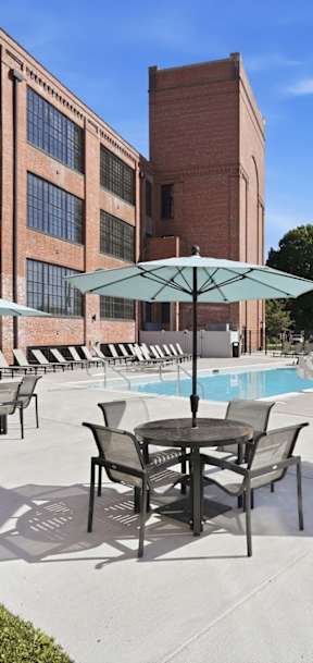 A pool area with chairs and umbrellas in front of a brick building.