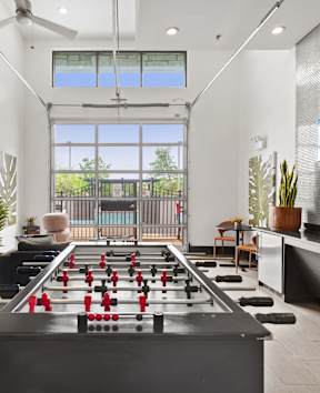 A foosball table is in the middle of a room with a chair and a plant.