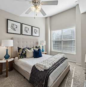 A bedroom with a large bed, a ceiling fan, and a window with blinds.