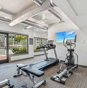 A gym with treadmills, elliptical machines, and a flat screen TV.