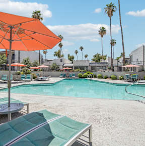 A pool area with a large orange umbrella and lounge chairs.