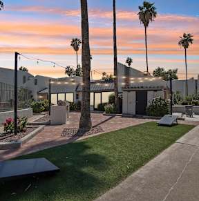 A sunset view of a courtyard with palm trees and a building in the background.