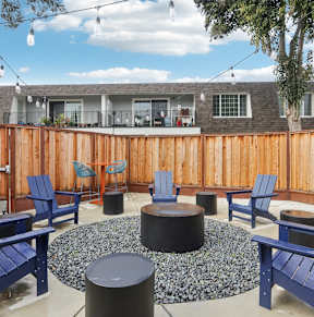 A patio with blue chairs and a fire pit.