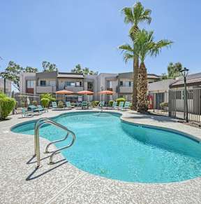 A large swimming pool surrounded by a concrete patio and a metal fence.