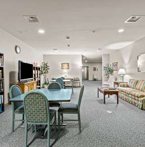 A living room with a grey table and chairs, a sofa, a bookshelf, and a TV.