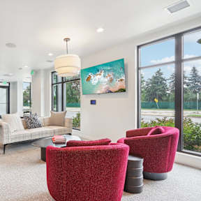 A living room with a white couch, red chairs, and a painting on the wall.
