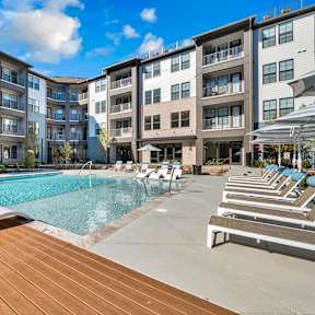 A large swimming pool with lounge chairs is surrounded by apartment buildings.