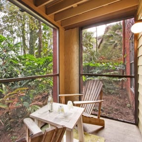 two chairs and a table on a screened in porch with a view of the forest