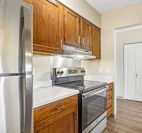 Irvine Park Towers kitchen with stainless steel range, wood cabinetry and doorway to the apartment interior