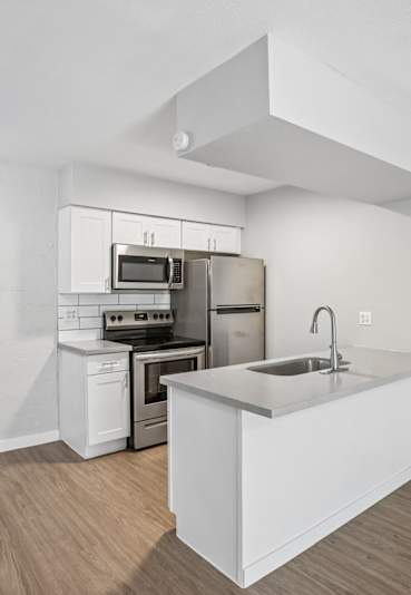 A modern kitchen features white cabinets, stainless steel appliances, a gray countertop island with a sink, and a white subway tile backsplash.