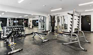 A gym with a variety of equipment including a bench press, a squat rack, and a leg press machine.