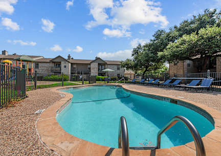 A small pool surrounded by a black fence and a few chairs.