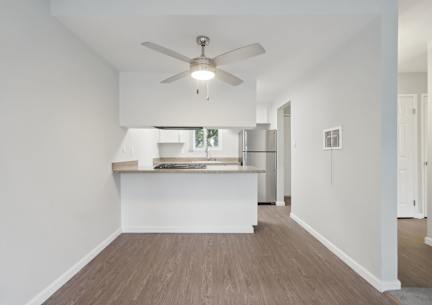 A room with a ceiling fan and a kitchen island in the background.