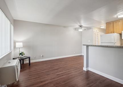 an empty living room with a kitchen and a ceiling fan