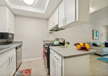 a renovated kitchen with white cabinets and appliances and a living room with a couch