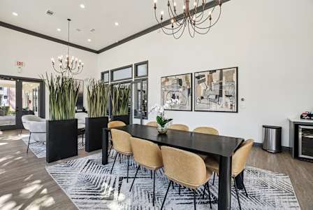 A black dining table with six chairs and a chandelier hangs above it.